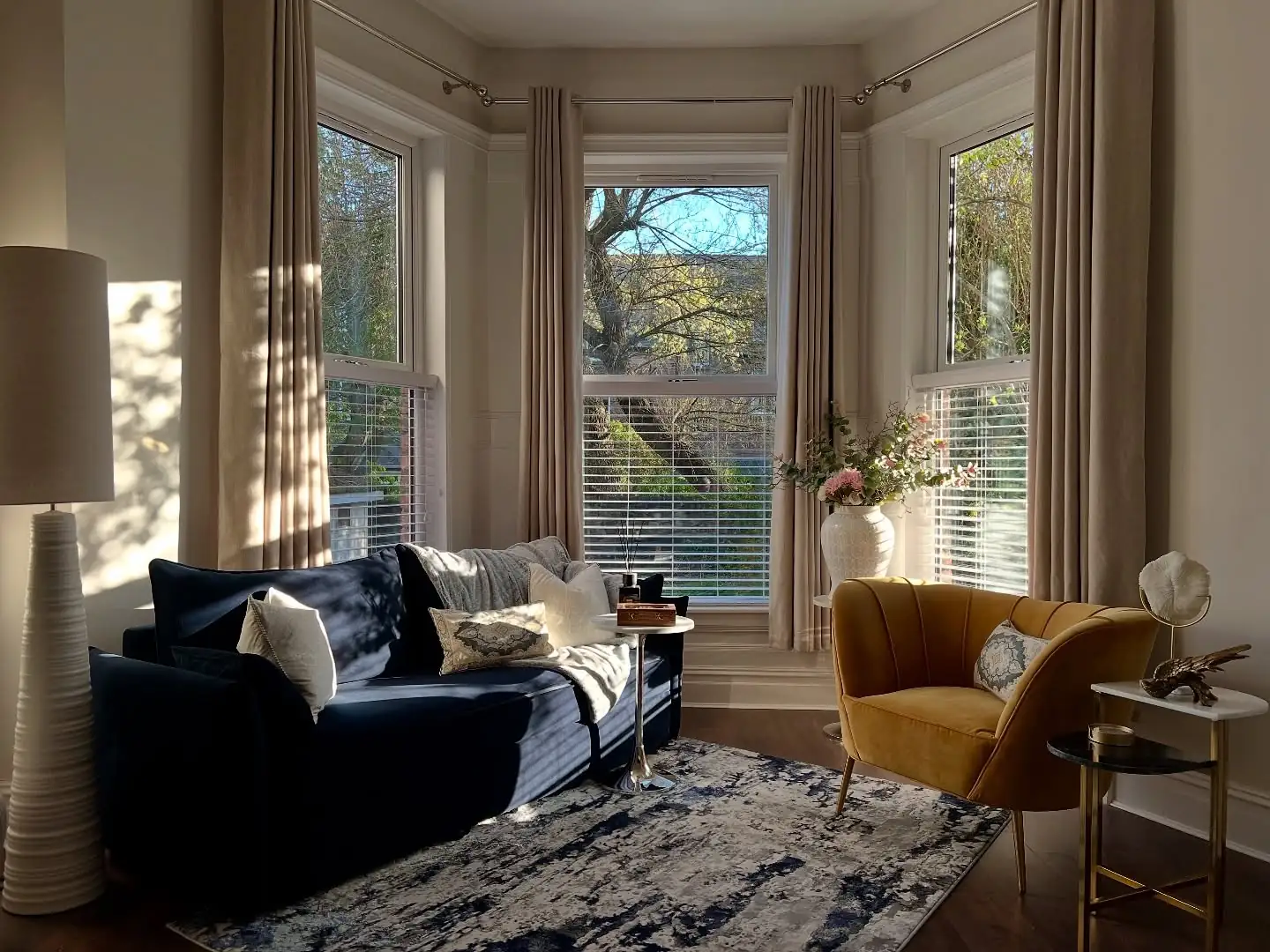 Bay window lounge with a navy sofa and mustard chair in afternoon sun