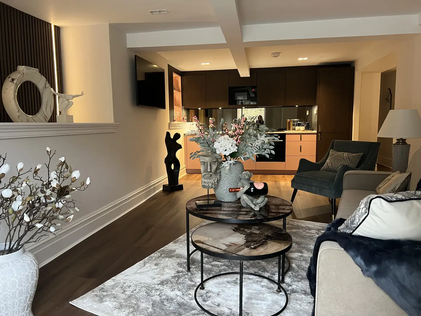 Open-plan lounge and kitchen with round coffee tables and a sculpture on the shelf